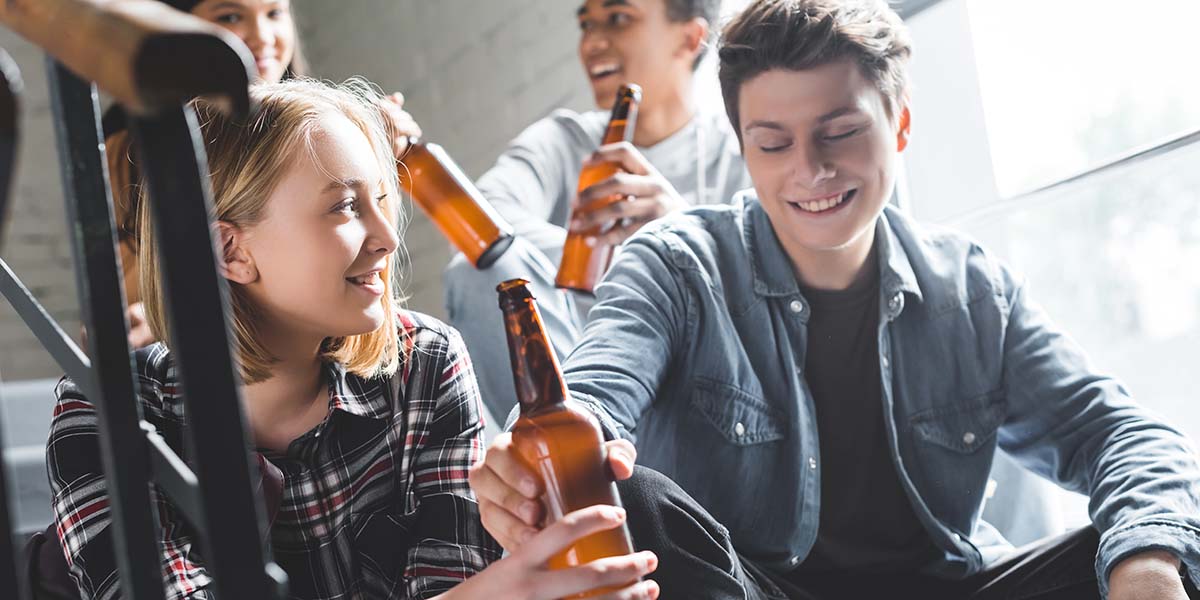 Smiling,Teenagers,Sitting,On,Stairs,,Drinking,Beer,And,Talking