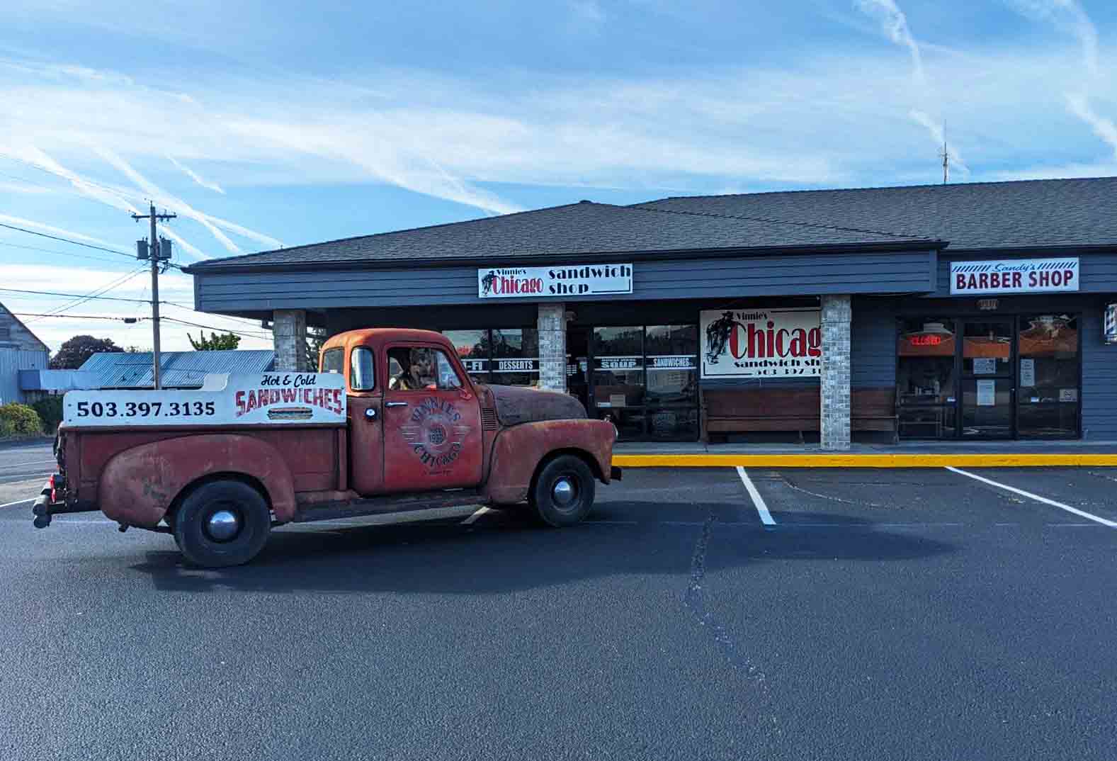 Photo via the Vinnies Chicago Sandwich Shop Facebook page. A vintage red truck sits in front of Vinnie's Chicago Sandwich Shop on a sunny day in St. Helen's Oregon.