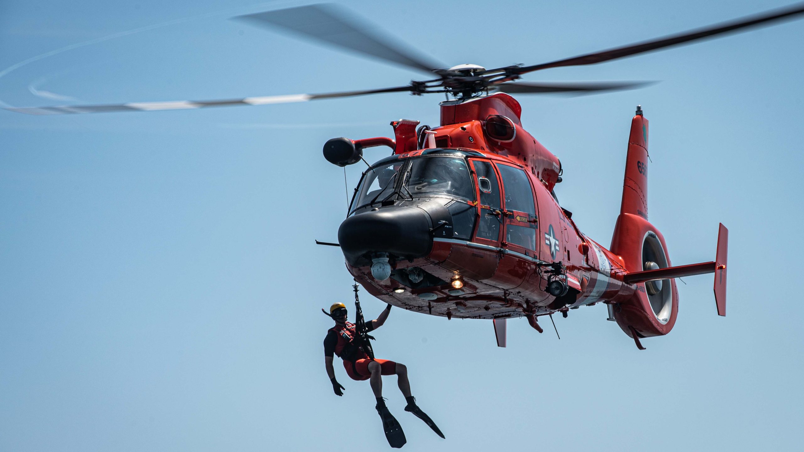 A U.S. Coast Guard (USCG) rescue swimmer hangs of the side of an coast guard rescue