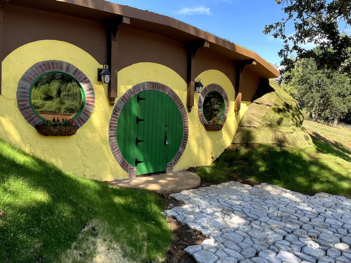 The Bag Inn, Lord of the Rings Airbnb in Oregon. The Bag Inn sits inside a hill. Cobbles lead up to the large green front door. The front of the building is yellow and brow. It looks like a hobbit home.