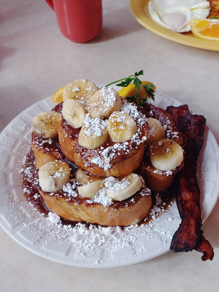 French Toast with bananas topped with powdered sugar. There's bacon on the plate as well. Looks tasty!