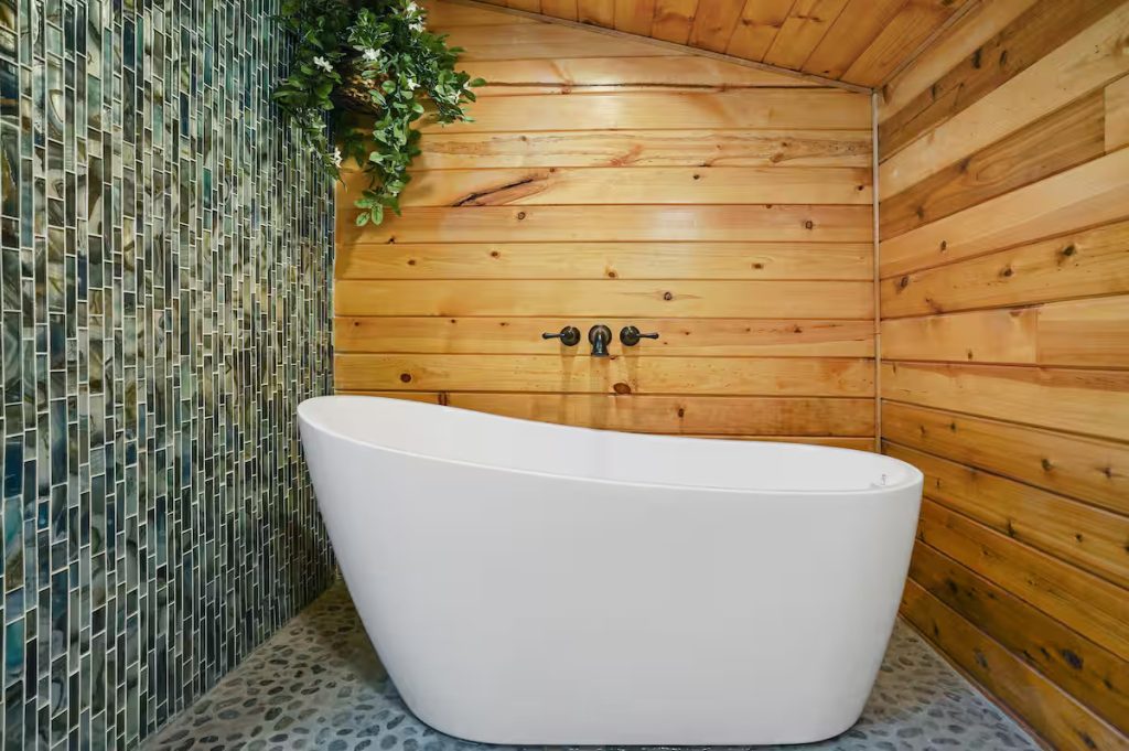 A huge white soaking tub in front of a wooden wall with a cobble floor. It looks like a spa.