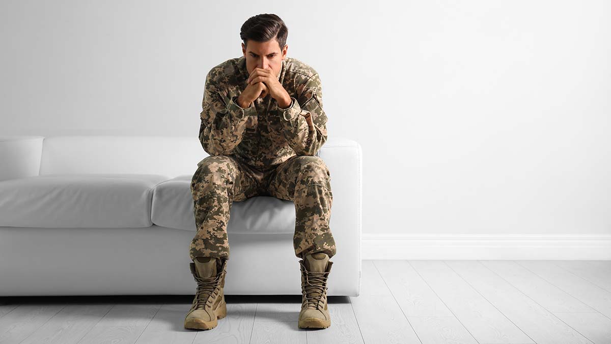 Stressed,Military,Officer,Sitting,On,Sofa,Near,White,Wall,Indoors. Sad National Guard troop