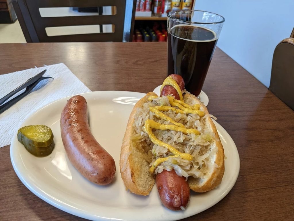 German sausage served on a roll with sauerkraut and mustard alongside a dark beer at a Portland deli