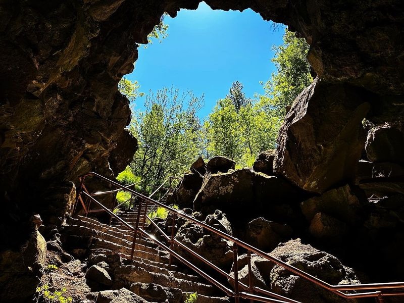 Stone staircase leading out of Lava River Cave entrance with blue sky visible above volcanic rock opening