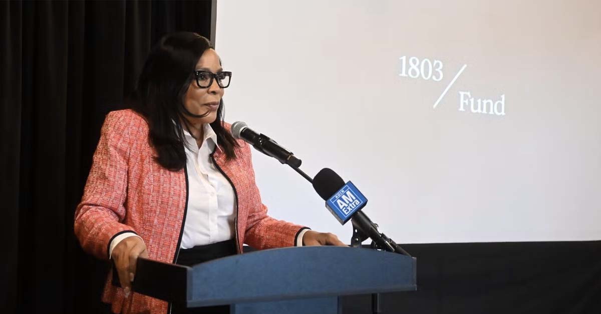 loretta-smith Portland Councilor Loretta Smith speaking at a podium with microphone during a public event, presentation slide visible behind her reading “1803 Fund”
