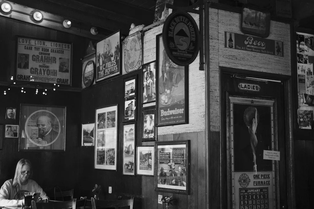 A black and white photo of a person sitting inside Goose Hollow Inn. Historic photos line the walls.