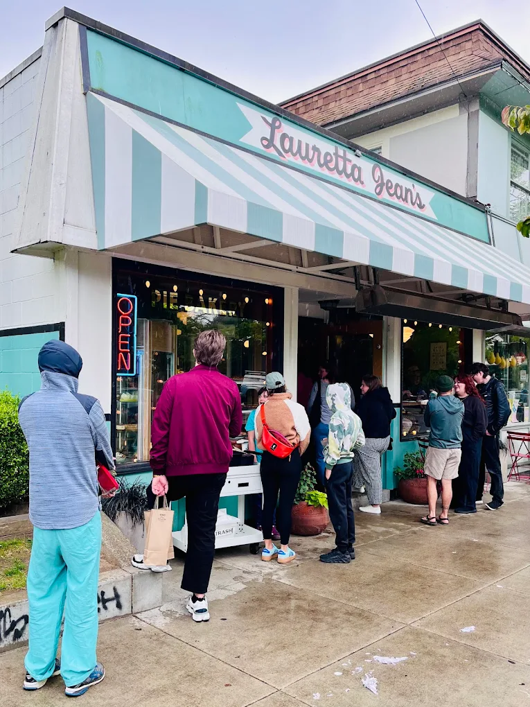 The outside of Lauretta Jean's. It's cute light blue and has a striped blue and white awning. This photo shows a line of people outside.
